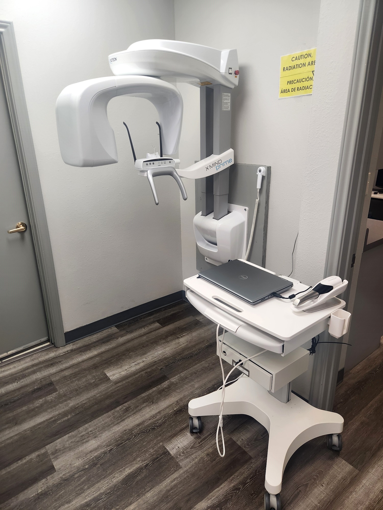 White walls with grey baseboards and trim work and door. Wood-look flooring. Portable x-ray machine.