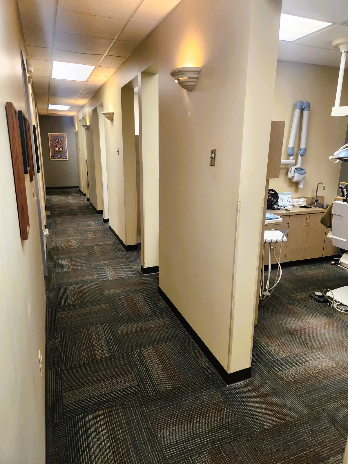 Tan walls with dark baseboards. Commercial carpet on the floor. Framed artwork and certificates like the wall down the hallway with doorways into the different rooms of the practice.