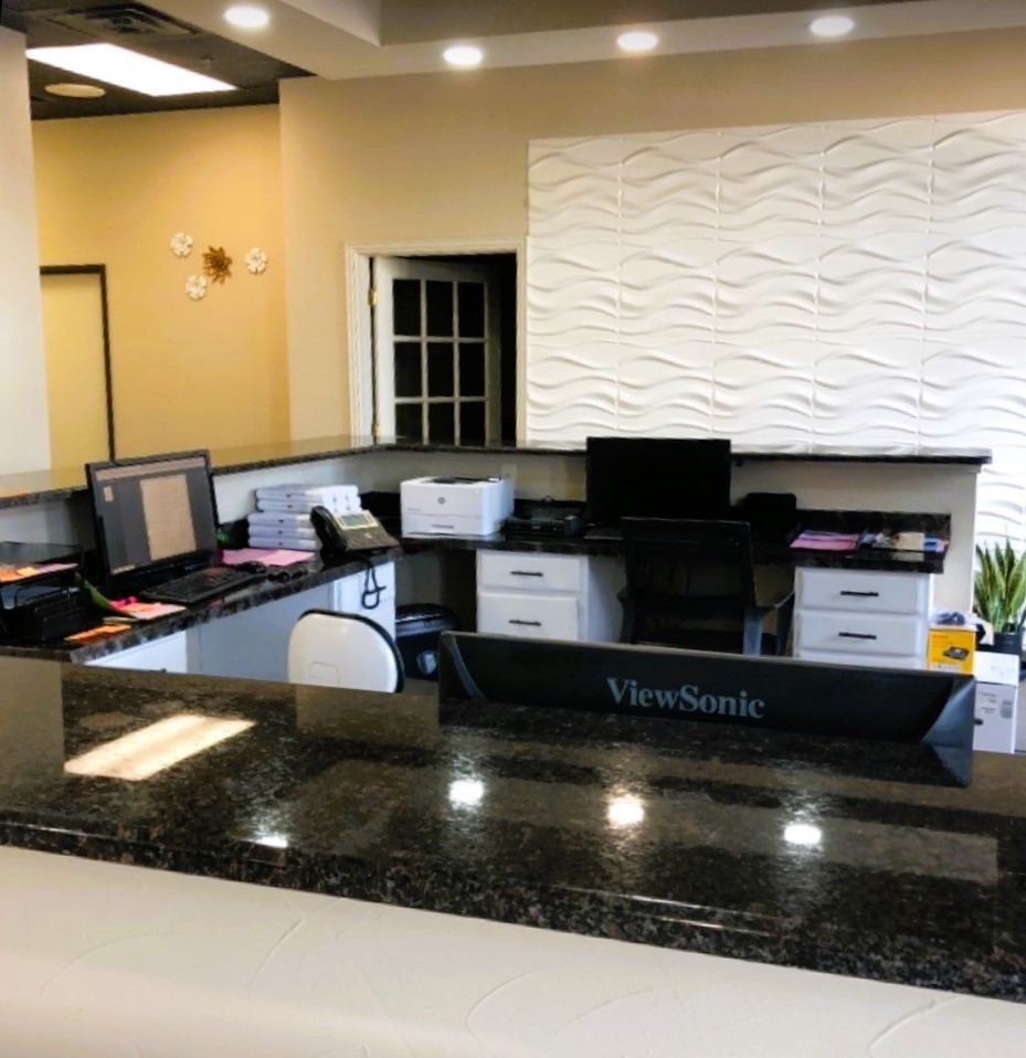 Light terracotta colored walls with dark trim with white floor to ceiling artwork on one wall. A large "C" shaped built in desk with a black granite countertops. It holds lots of office equipment, tools, and supplies. Black rolling office chairs.