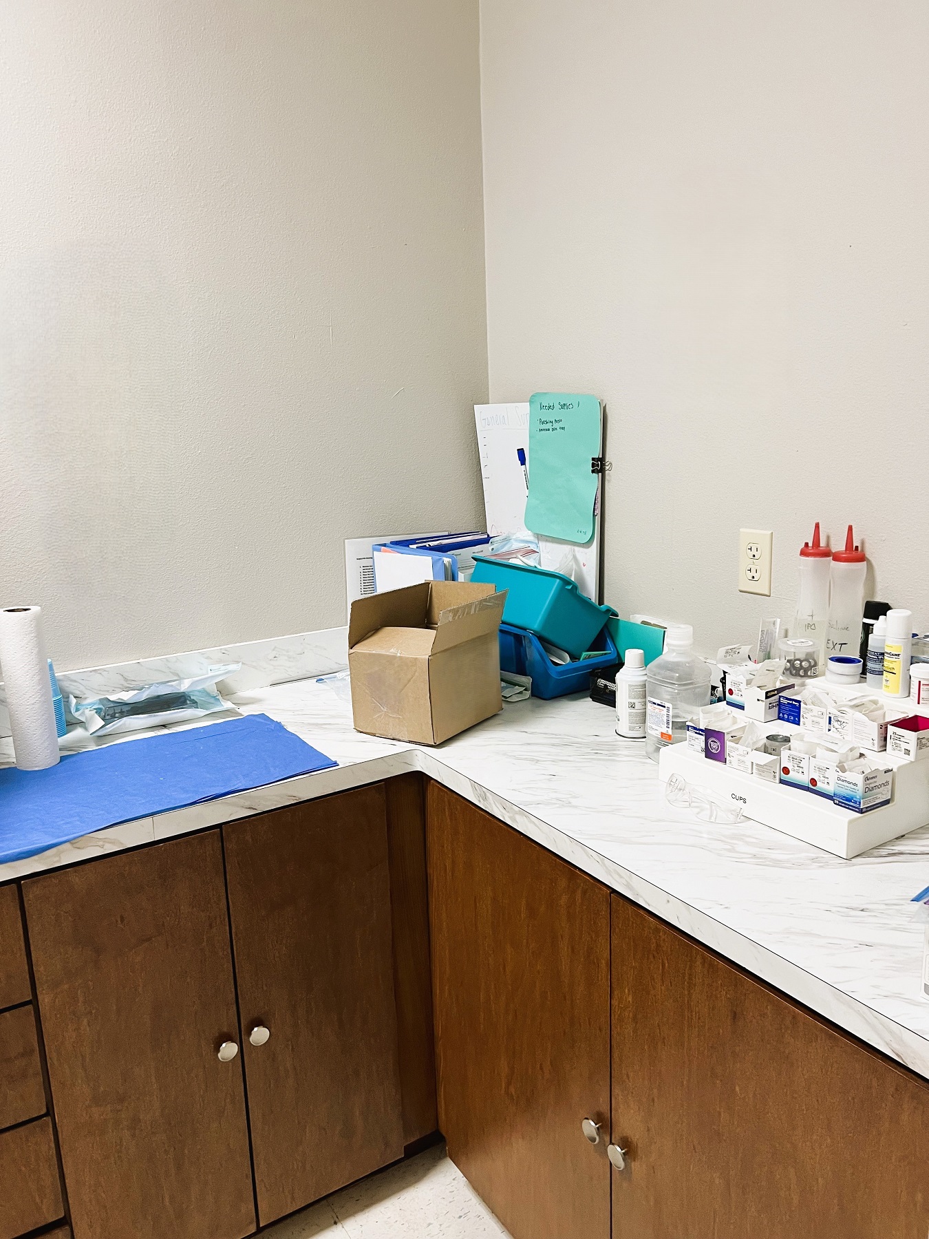 Light colored walls with dark baseboards and white, large, tile flooring. Dark stained cabinetry with light counter tops holds lots of dental sterilization tools, equipment, and supplies.