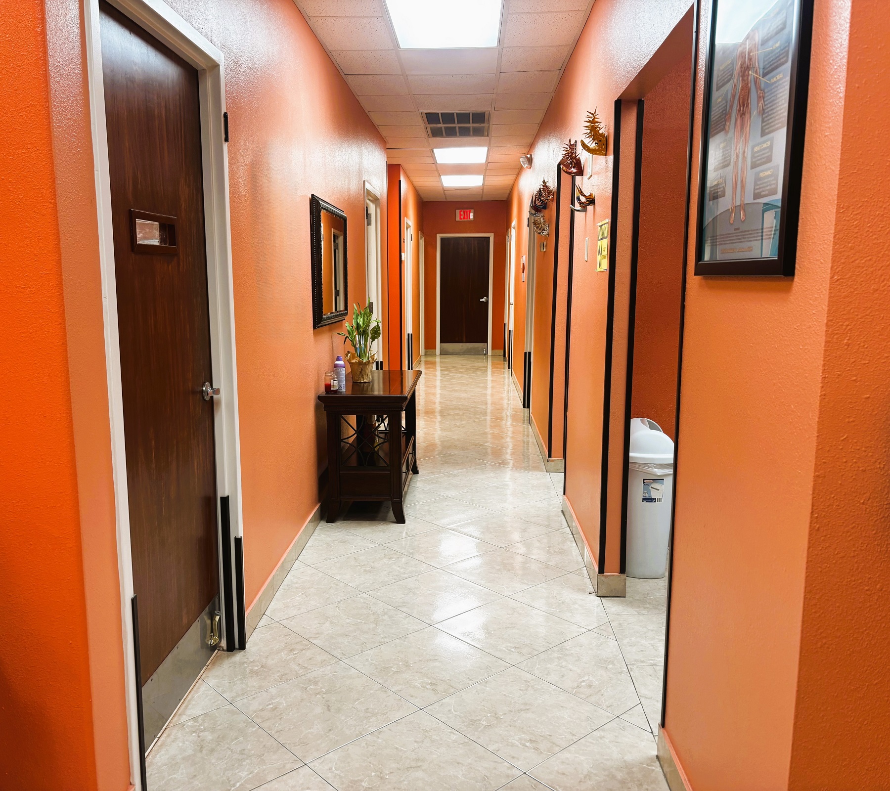 Bright and light colored walls with white trim and large grey tile flooring. Dark stained wood doors lead to the different rooms of the practice.