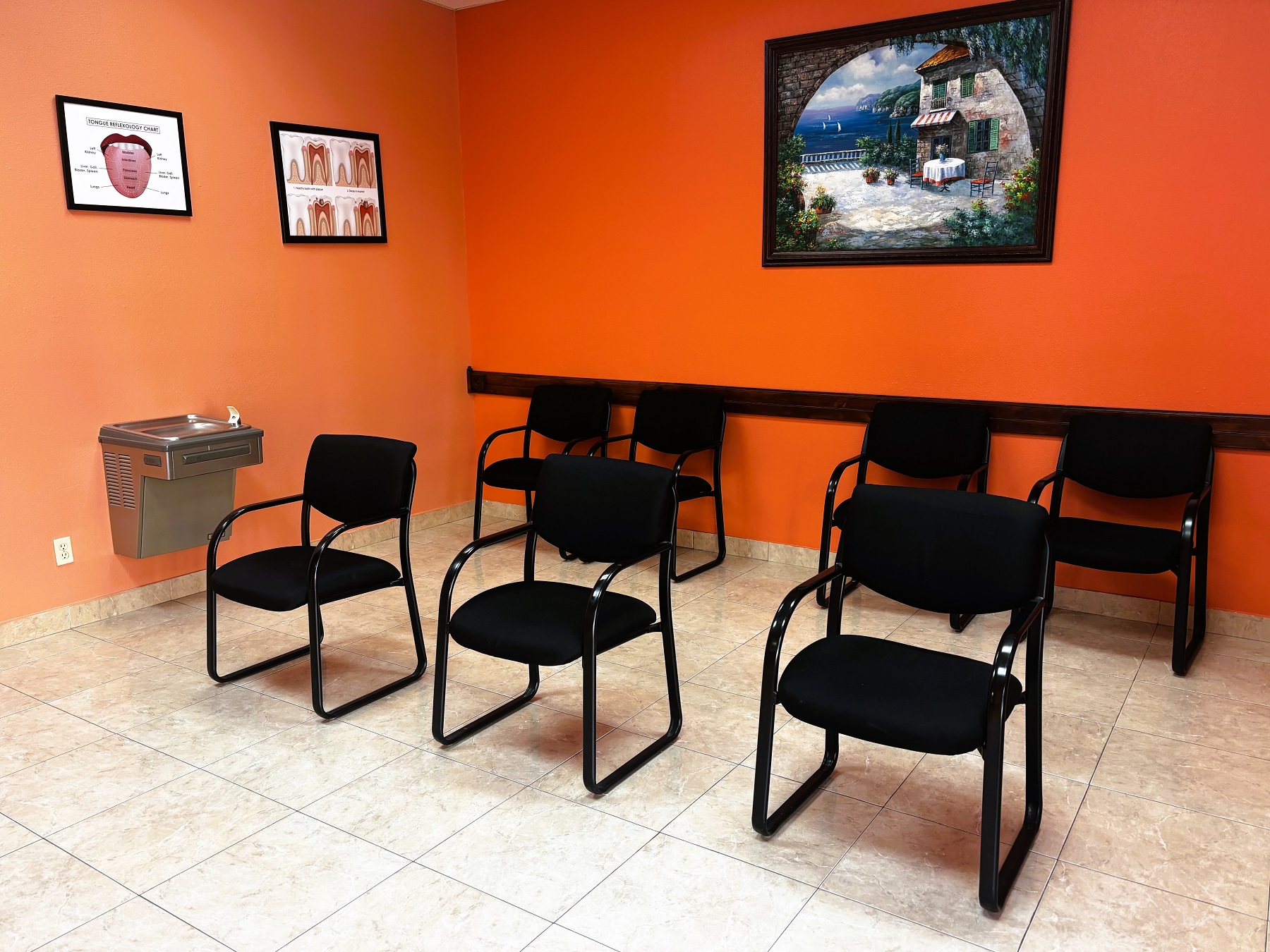 Bright and light colored walls with white trim and large grey tile flooring. Artwork is hung on the wall and black arm chairs are set up in two rows.