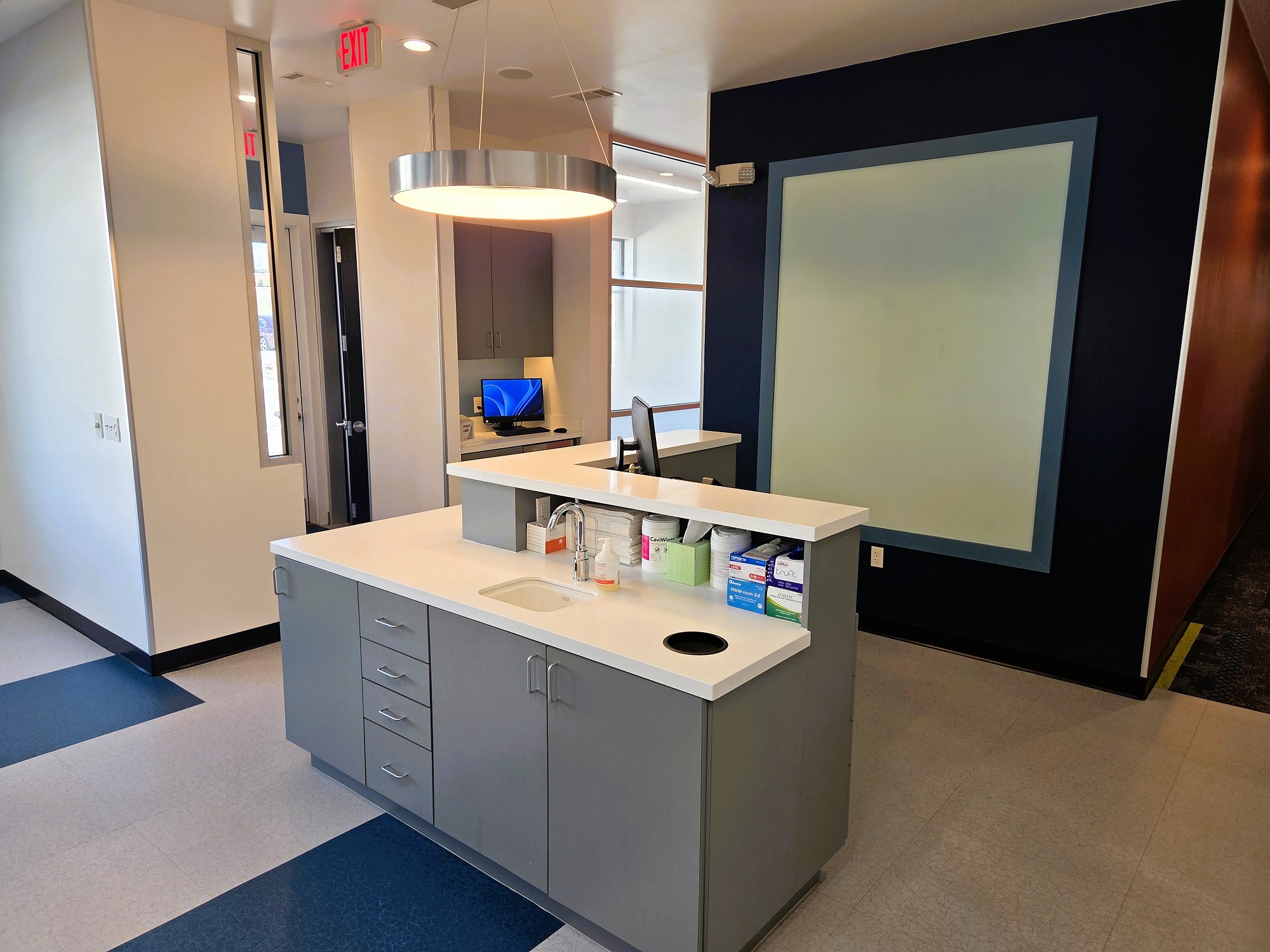 Light grey walls with black baseboards. Two tone epoxy floors that are flecked black and grey. Clinical station is builtin with a dark grey base and light grey countertops and a built in brushing station. Plenty of storage space included.