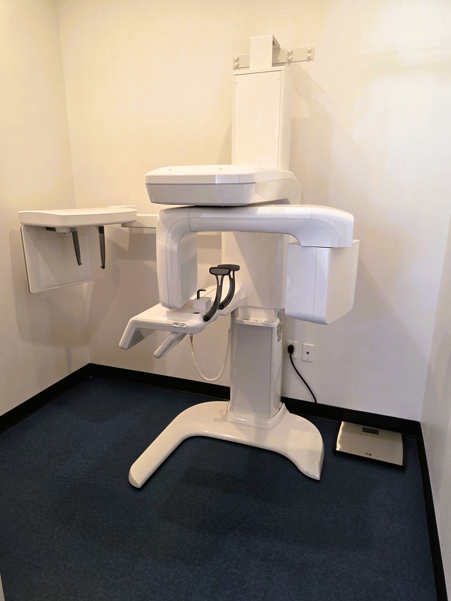 Light walls with dark baseboards and blue tile flooring. A large white dental x-ray machine stands against the wall.