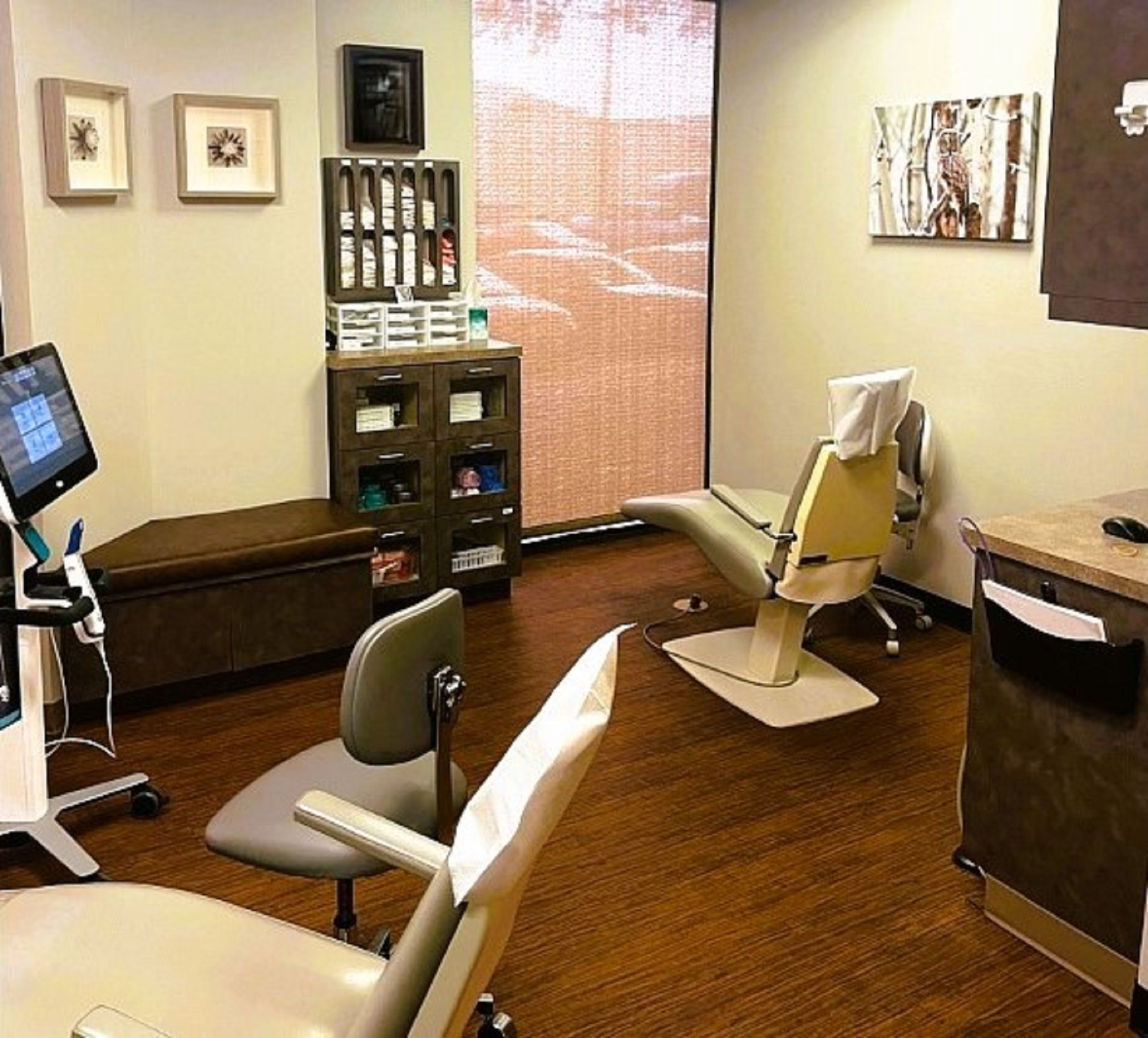Light walls with dark baseboards and dark brown commercial carpet tile flooring. A large floor to ceiling window is covered by a cloth blind. Dental procedural chairs with matching rolling chairs and equipment stands create a wonderful dental operatory.