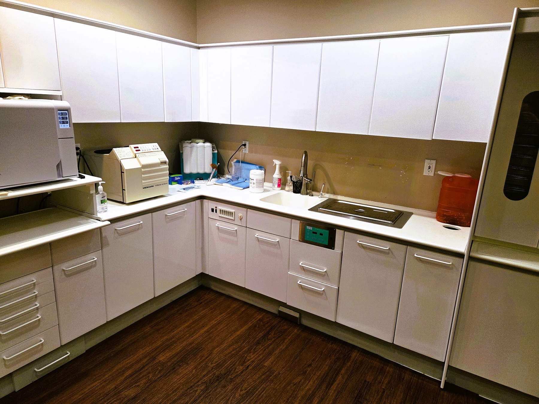 Beige walls with white cabinetry and countertops house lots of dental lab tool, equipment, and supplies.