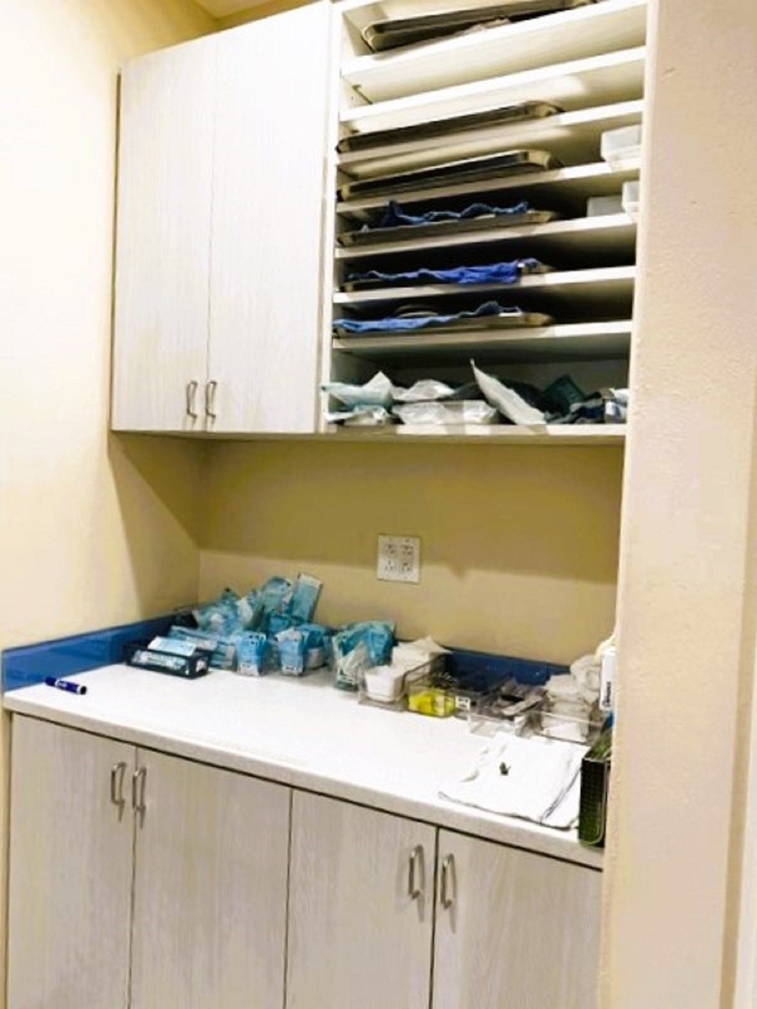 Beige walls with light grey cabinetry uppers and lowers with matching countertops and lot of shelving inside for supplies.