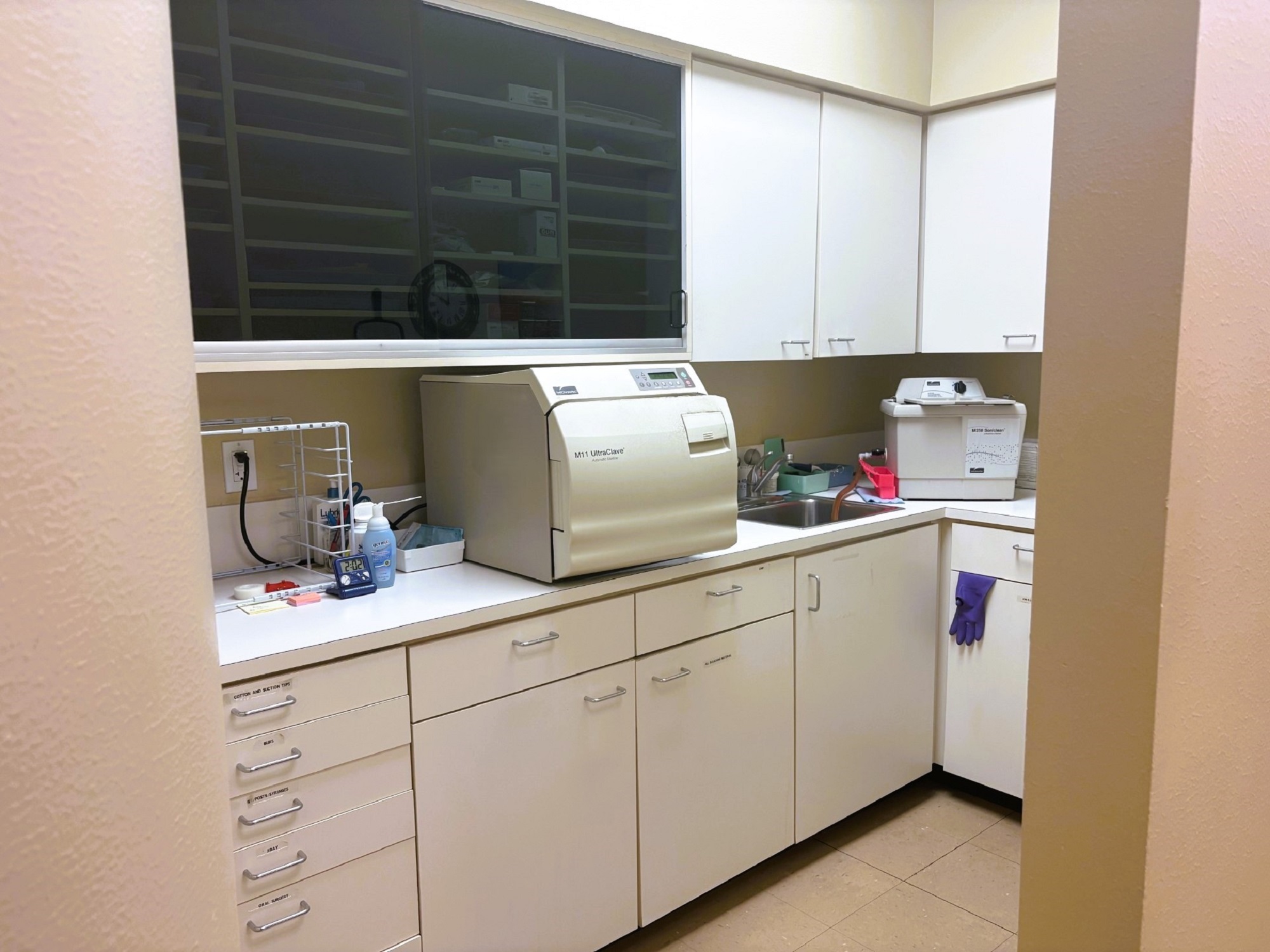 White cabinets with matching countertops. Tons of drawers and shelves for holding lots of tools, supplies, and equipment. Sterilization equipment sits on the countertop near a small stainless steel sink.