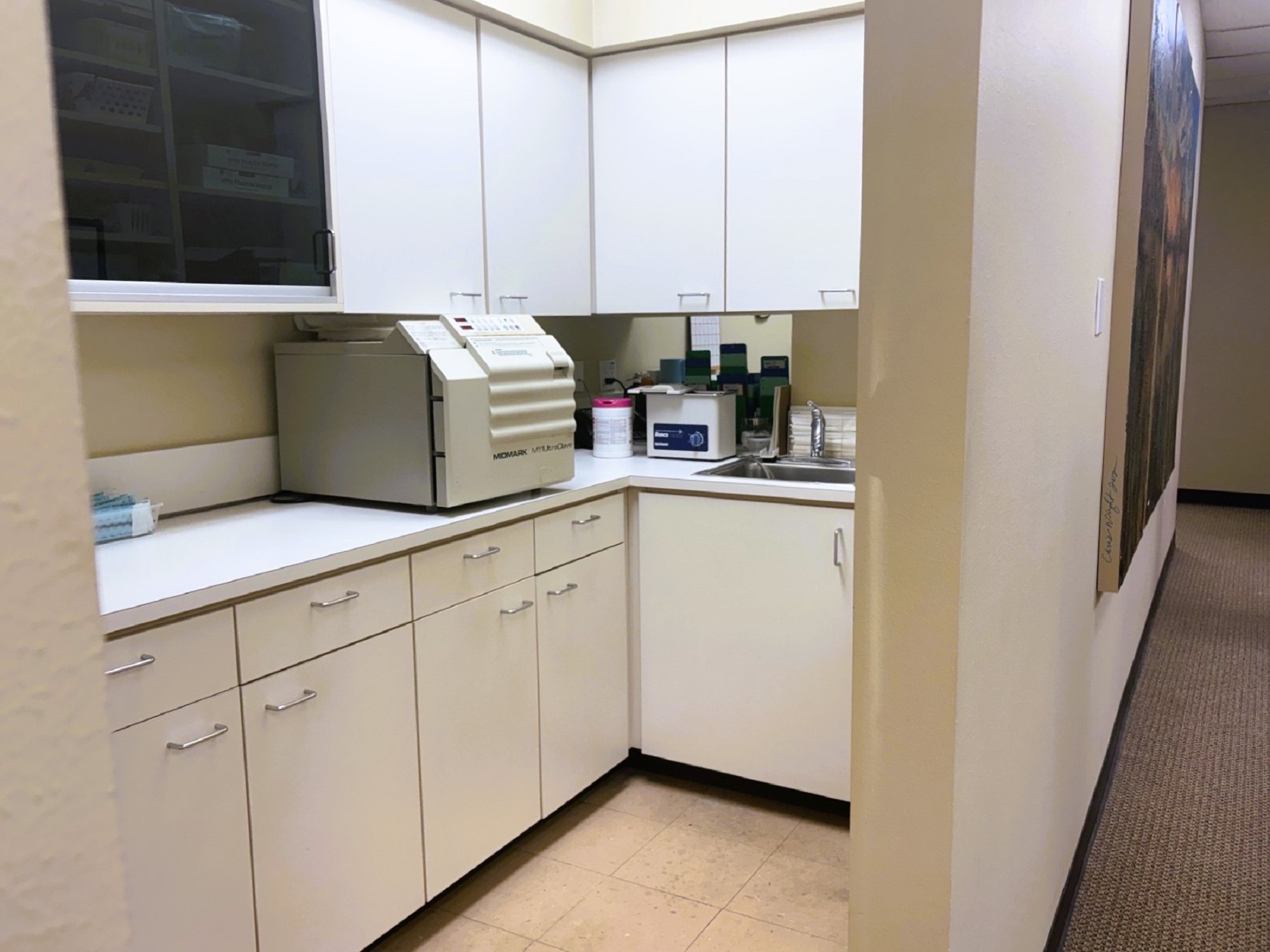 White cabinets with matching countertops. Tons of drawers and shelves for holding lots of tools, supplies, and equipment. Sterilization equipment sits on the countertop near a small stainless steel sink.