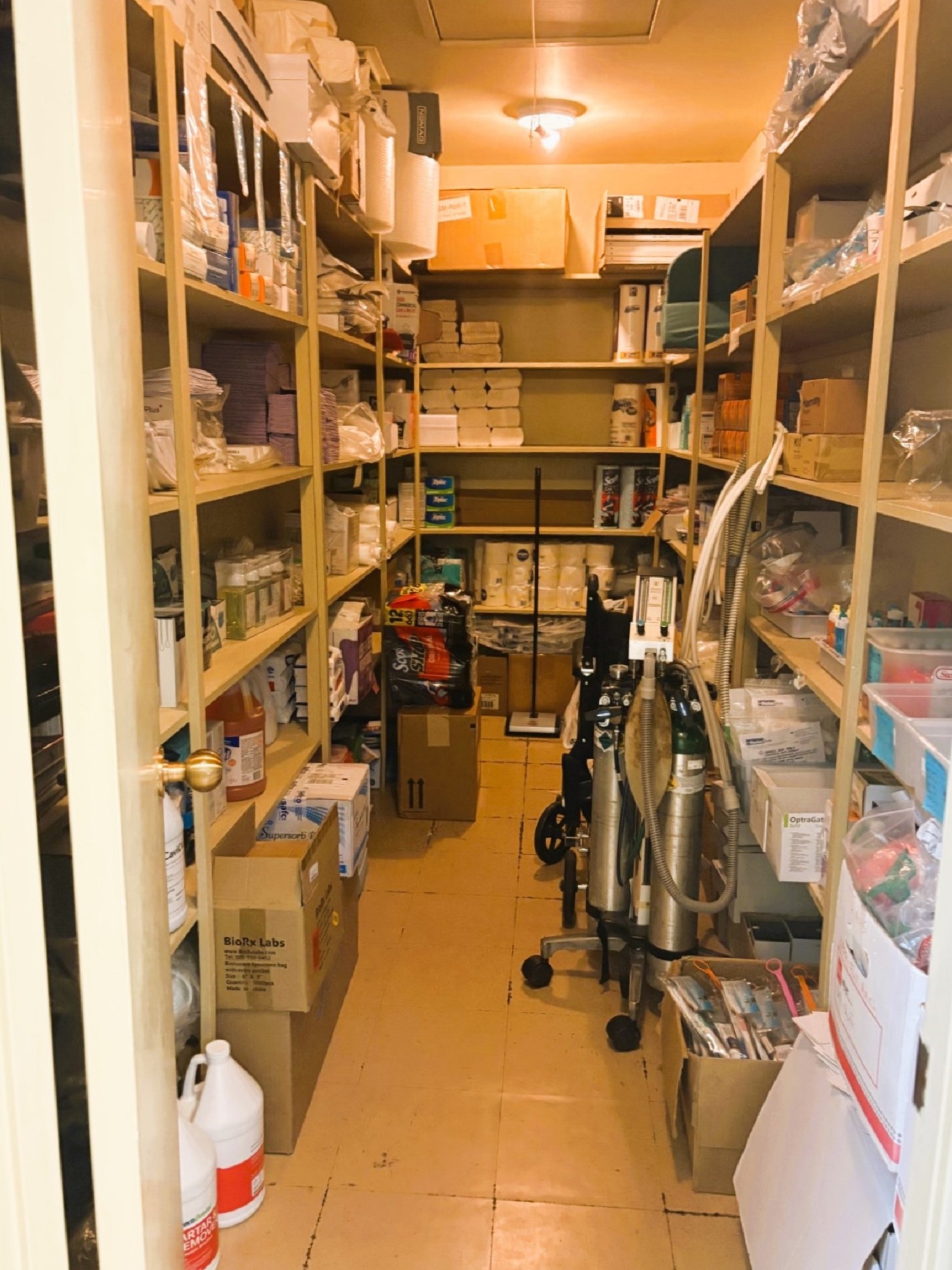 A small room with floor to ceiling and wall to wall shelving holds lots of dental supplies and equipment.